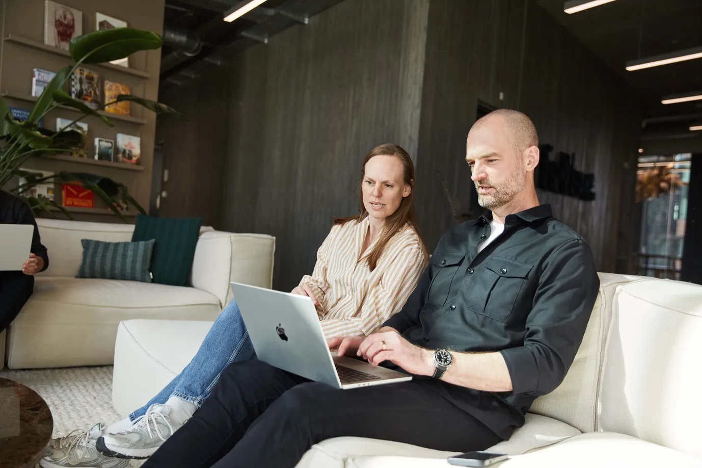To kolleger arbejder sammen i en sofa med laptops